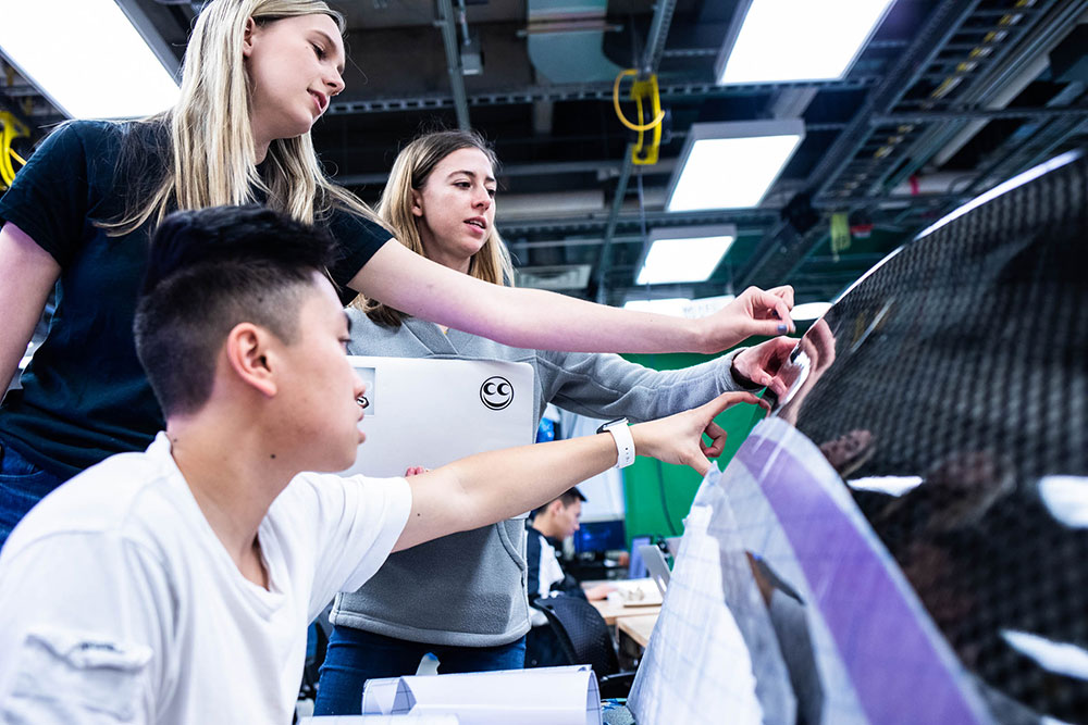 three students touching a carbon fiber pod 