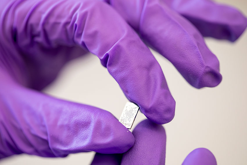 hand wearing purple gloves holding a silicon wafer