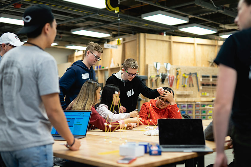 A group of middle schoolers sitting around a table constructing spaghetti and marshmallow structures