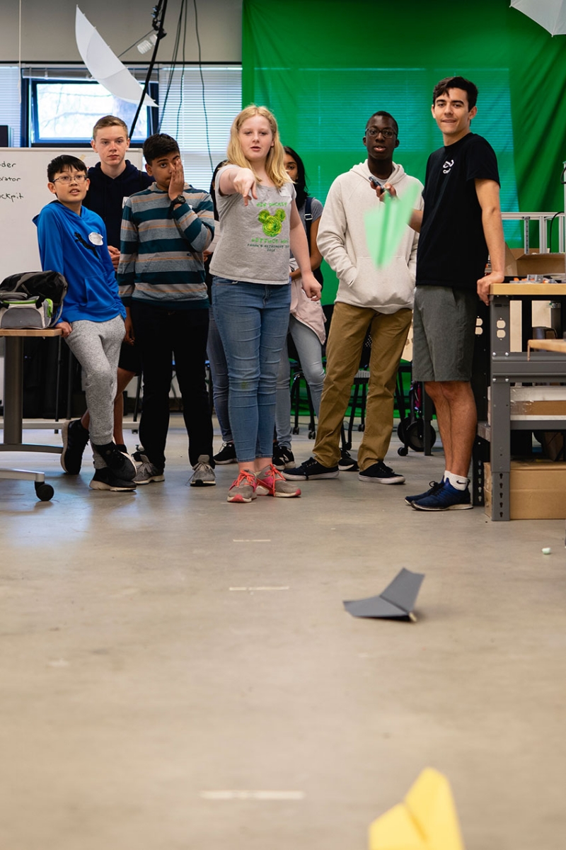 A student throws paper airplanes while a group of students look on