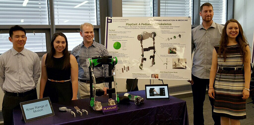 Students standing with a poster and model of PlayGait exoskeleton