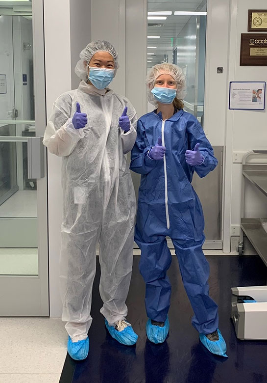 Two researchers in protective lab gear stand next to each other