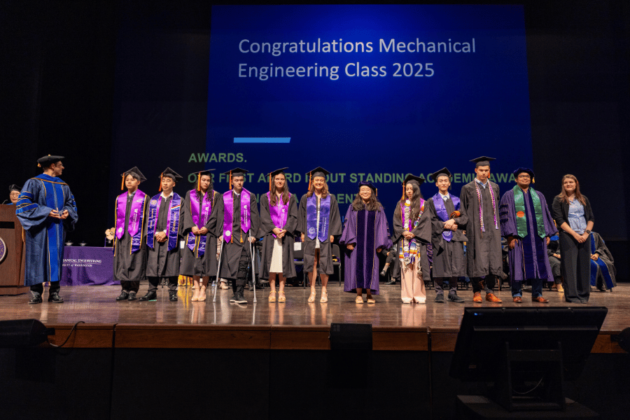 Two ME faculty stand with a group of 2025 graduates onstage.
