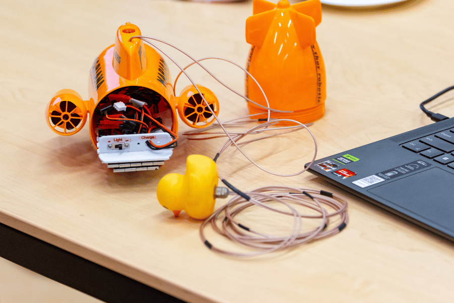 A small orange model of a submarine on a table. The submarine has wiring inside of it.