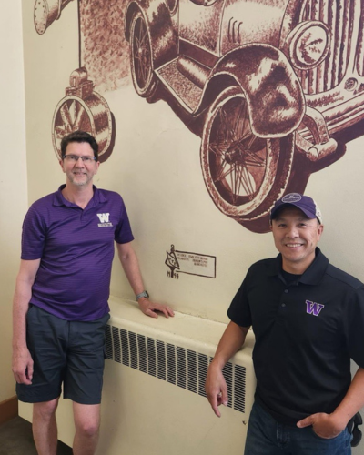 A close shot of two people stand in front of a mural in a stairwell.