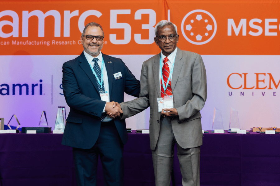 Two men shaking hands while looking at the camera.