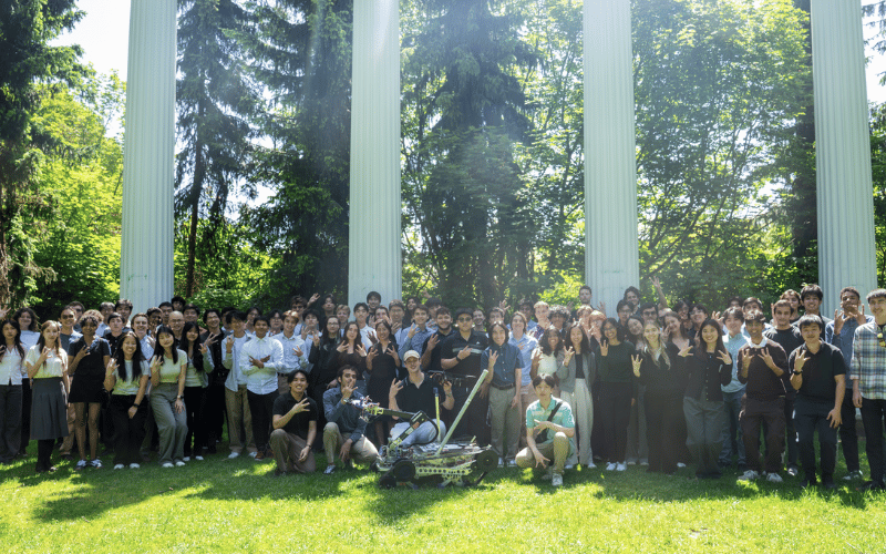 The Husky Robotics team stand with their rover in front of columns on the UW campus.