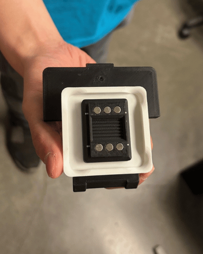 A hand holds a palm-sized device that includes a small tray in which tissue samples are placed.