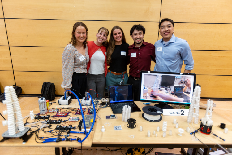 Five students stand behind a table showcasing pieces from their robotics project.