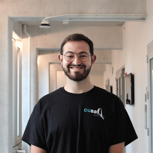 Headshot of Alex Eagan smiling in a hallway.