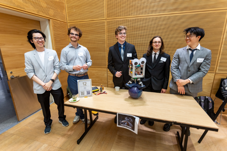 Five students stand behind their project, a robot with googly eyes balancing atop a ball.