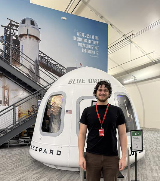 Connor Fallot stands in front of a part of a launch vehicle at the Blue Origin headquarters.