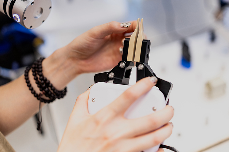 A student holds a device at the end of the robotic arm with a small gripper. 