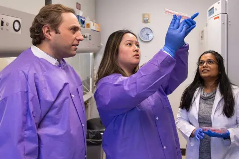 Three individuals in a lab examining a sample