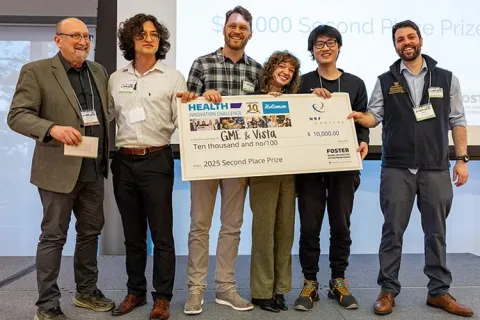 A group of six people on stage holding a large check for a competition prize