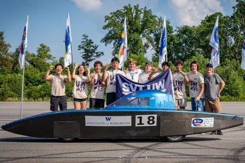 Team celebrating behind a solar-powered car with the number "18," displaying a "University of Washington" decal.