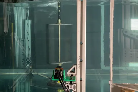 A transparent water tank with a vertical cylindrical apparatus inside, set in an industrial laboratory setting.