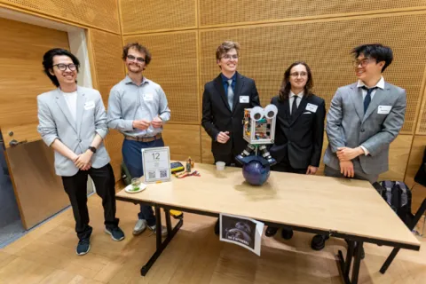 Five students stand behind their project, a robot with googly eyes balancing atop a ball.