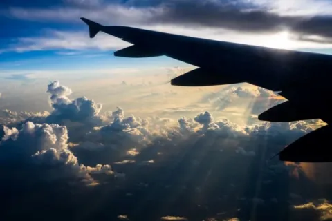 View from an airplane window showing a wing and a sky filled with clouds and rays of sunlight.
