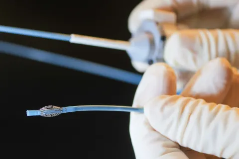 Gloved hands hold a catheter device.