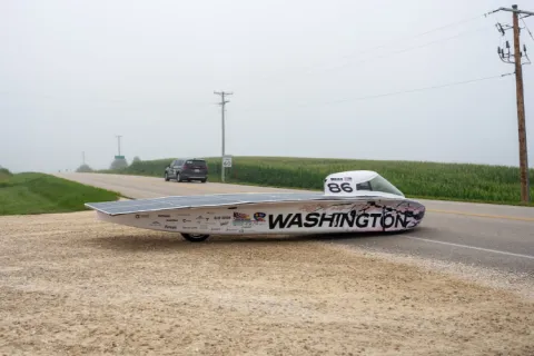 The solar vehicle car with cherry blossoms painted on it on a street with grassy fields.