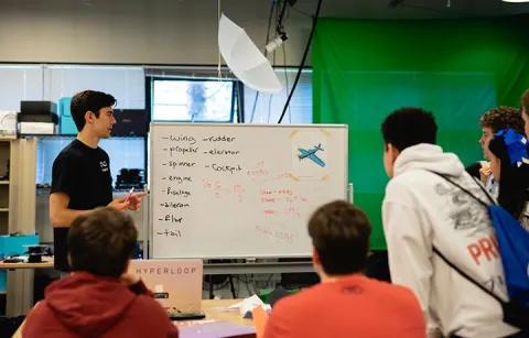 ME student standing next to a whiteboard with school students in the audience