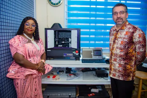Two people pose beside a 3D printer and a laptop on a desk
