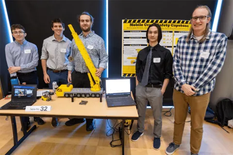 A group of five people stand behind a table with a crane model and laptops