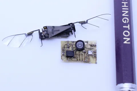 A sensor suite next to an insect robot with wings and part of a pencil for scale