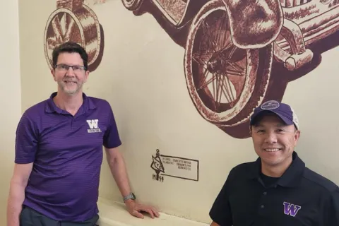 A close shot of two people stand in front of a mural in a stairwell