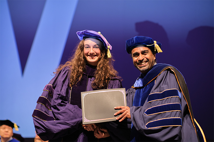 Woman smiling to camera while receiving diploma during graduation ceremony