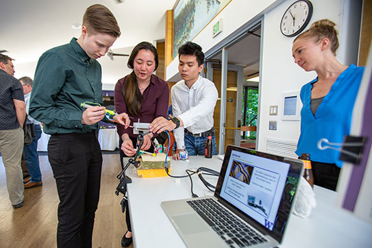 group of people engaged in a demonstration at a tabletop exhibit with a laptop and equipment.