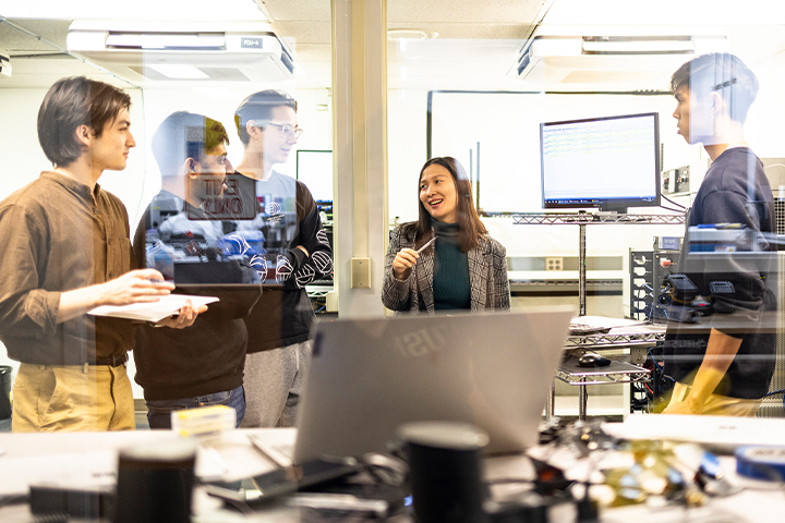 People engaging in conversation behind the glass wall of a lab