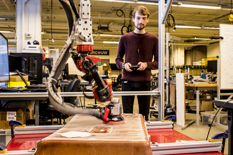 Man standing in a lab using a controller to operate a robot