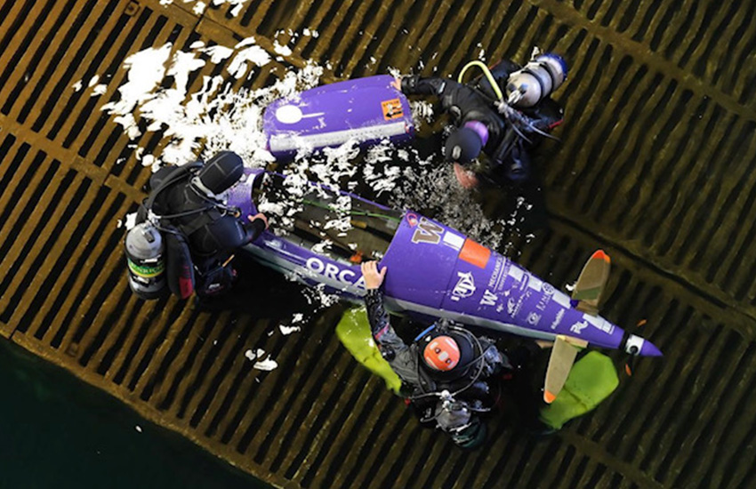 Three members of the UW Human Powered Submarine team are pictured in the water surrounding their submarine in a photo taken from above.