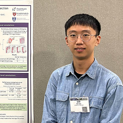 Gan Gao smiles and stands next to a poster