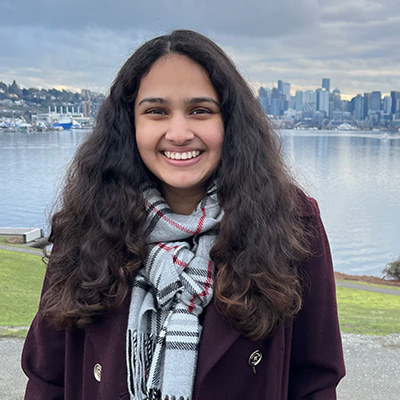 Niharika Karnik smiles and stands in front of a lake and a skyline