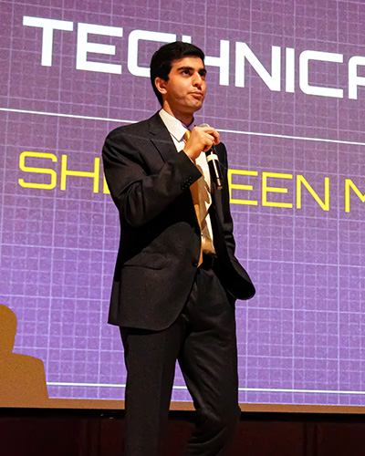 Sherveen Mehrvarzan wearing a suit and holding a microphone.