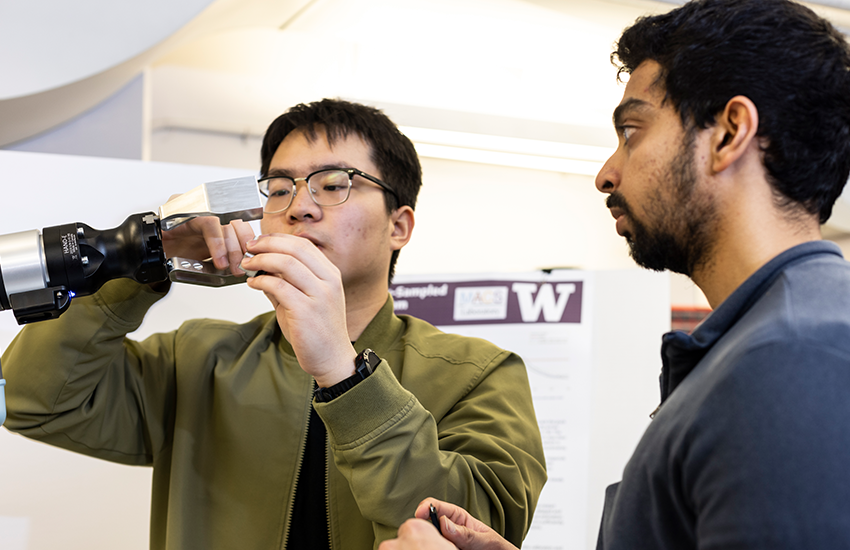 Two student researchers adjust a robotic gripper.