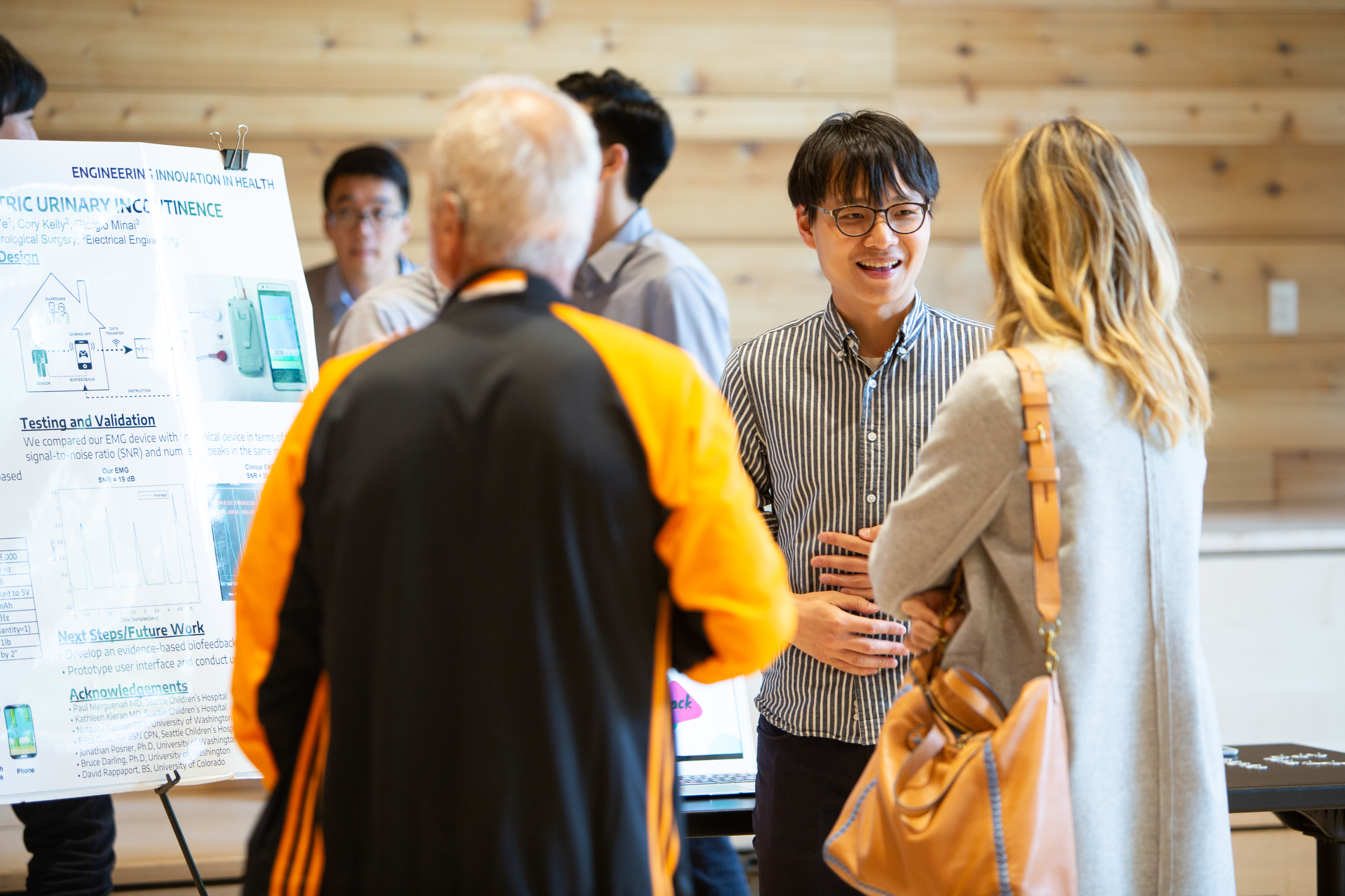 Students speaking to a group of people in front of project poster