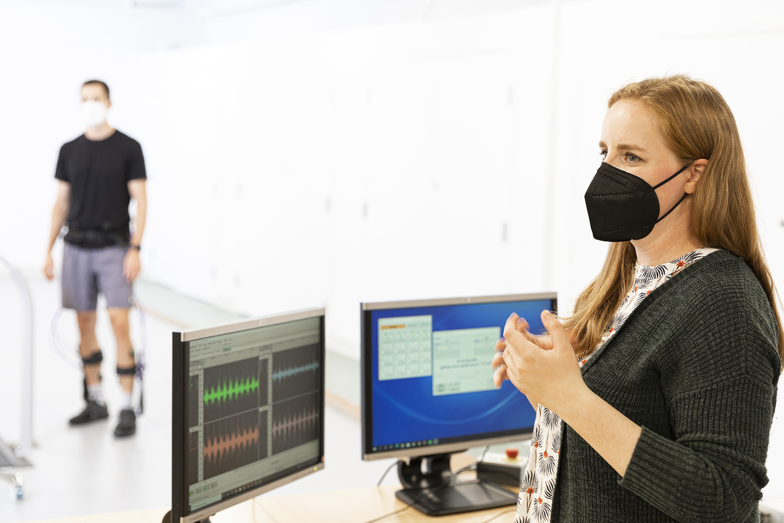 Female researcher at a lab talking and standing next to two monitors displaying data