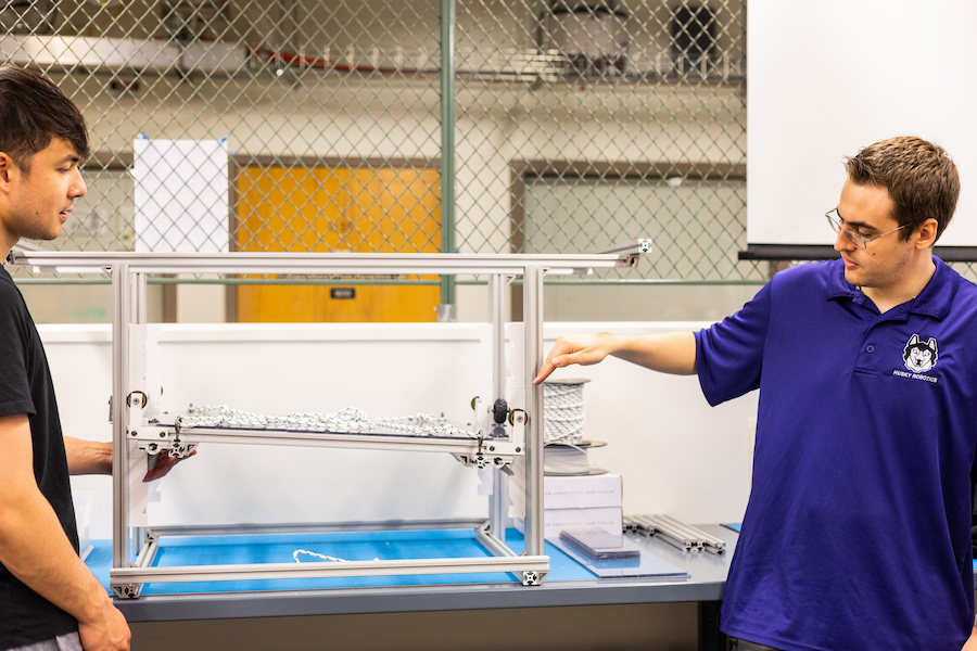 Two students at a lab showing a scale model of a test load tower