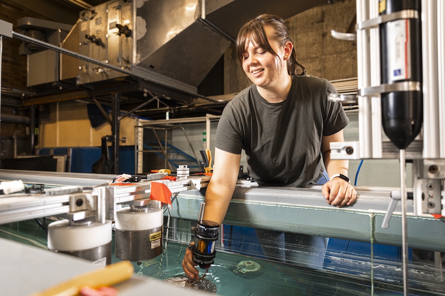 Woman standing next to a metal railing, placing an object inside a flume at the Harris Hydraulics Lab