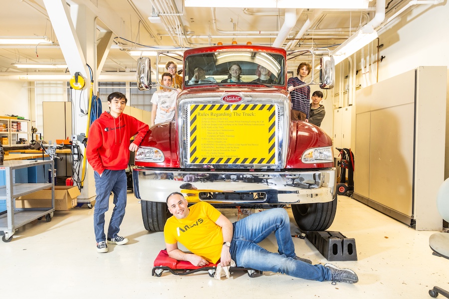 Nine members of the club's structures sub-team pose around the truck, which has a bright yellow sign with rules on it.