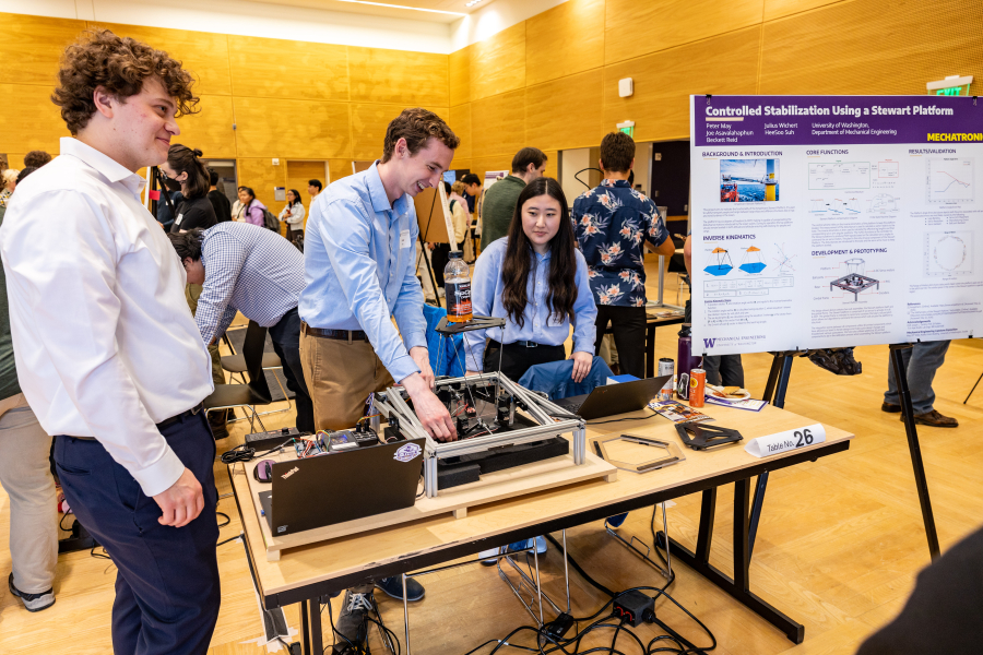 Three students next to a table that holds a platform with a plastic bottle on top.