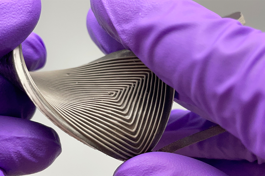 Close up of hands with purple gloves holding a small and stretchable generator that converts body heat to electricity.