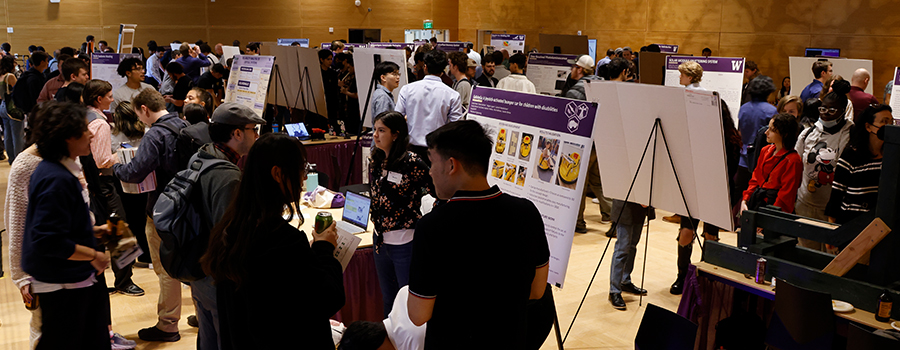 A crowded room with people discussing and viewing poster presentations at an exhibition.