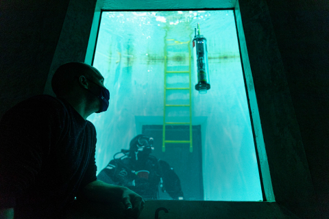 Trevor Harrison looking through the glass pane of a big water tank with a diver and a µFloat inside