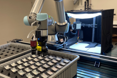 A robot arm is positioned over a case full of a set of identical metal parts arranged in a 7x5 array.