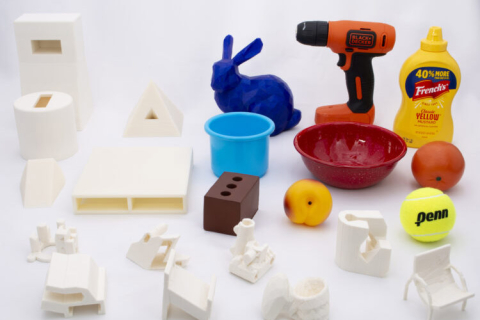 22 objects on a table top. Objects include white 3D printed shapes and also random household items such as a drill, a mustard container, a bowl and a tennis ball